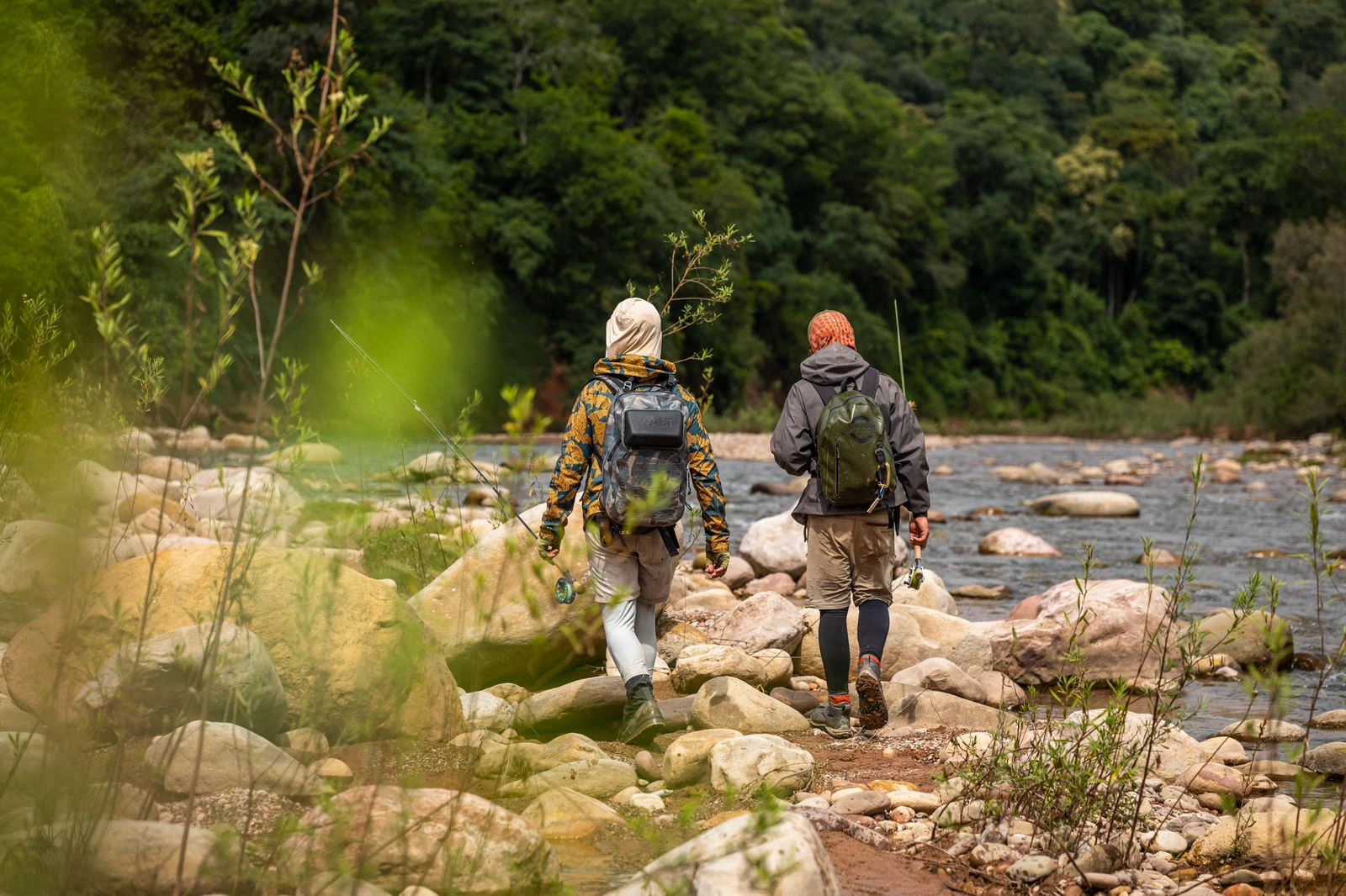 Dos participantes recorren la orilla entre rocas y vegetación.